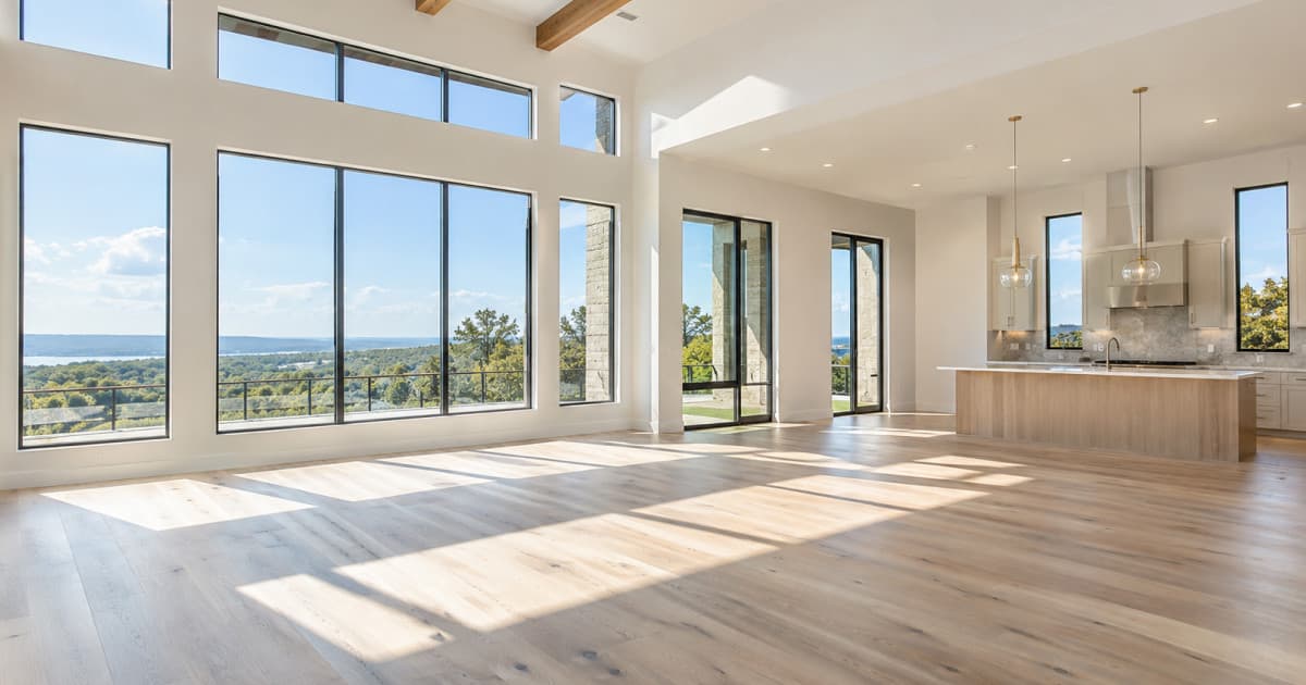 Sunlit open-plan living room with floor-to-ceiling windows and light wood floors